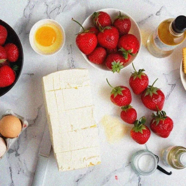 Fresh ingredients for homemade strawberry cheese cake arranged on marble surface, including cream cheese, strawberries, and baking essentials