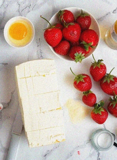 Fresh ingredients for homemade strawberry cheese cake arranged on marble surface, including cream cheese, strawberries, and baking essentials