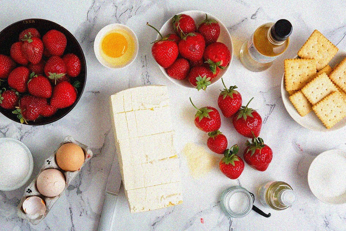 Fresh ingredients for homemade strawberry cheese cake arranged on marble surface, including cream cheese, strawberries, and baking essentials